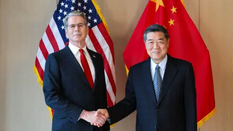 Líderes de Estados Unidos y China estrechan la mano con las banderas de ambos países de fondo